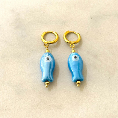 Pair of blue fish-shaped earrings with gold accents on a beige background