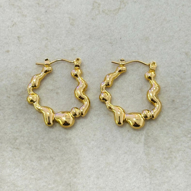 Gold wavy hoop earrings on a light gray background