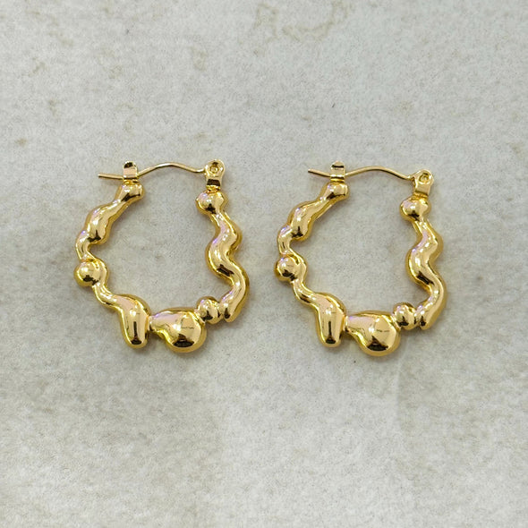 Gold wavy hoop earrings on a light gray background