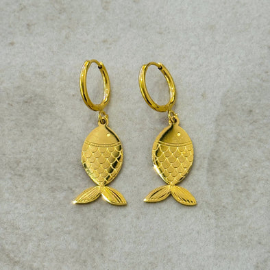 Gold fish-shaped earrings on a textured gray background