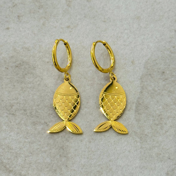 Gold fish-shaped earrings on a textured gray background