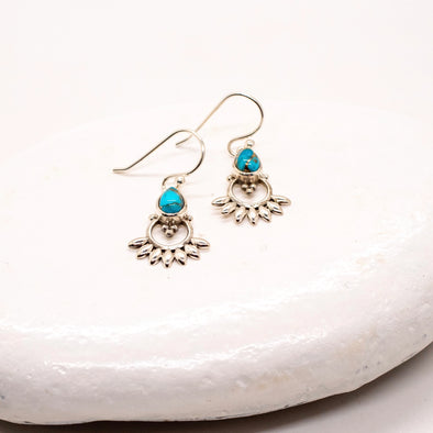 Silver earrings with turquoise stones on a white stone surface