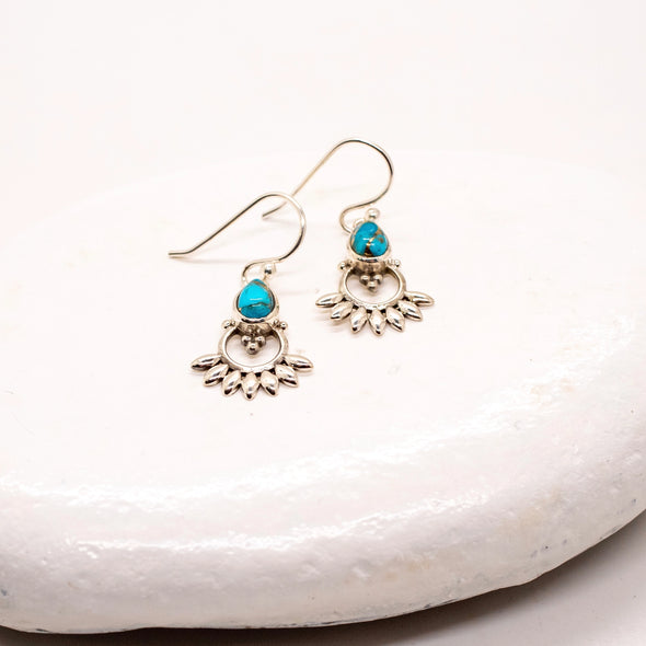Silver earrings with turquoise stones on a white stone surface